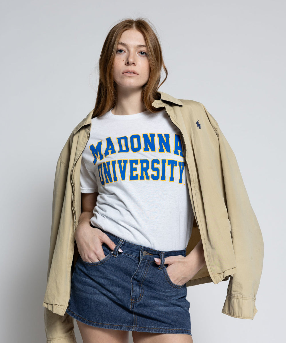 Person wearing a white t-shirt with 'MADONNA UNIVERSITY' text, denim shorts, and a beige jacket on a plain background
